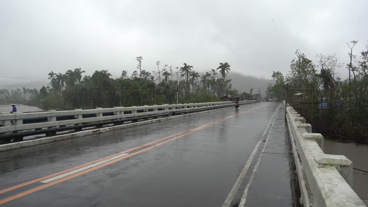 Motorcycle Driving On Road Bridge Amidst Heavy Rainfall During Typhoon Odette In Southern Leyte, Philippines. wide shot