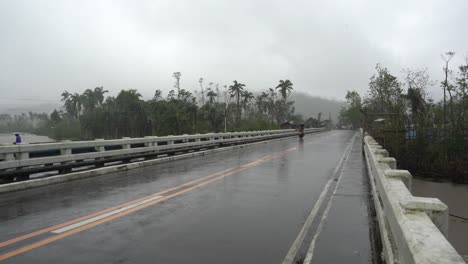 motorcycle driving on road bridge amidst heavy rainfall during typhoon odette in southern leyte, philippines. wide shot