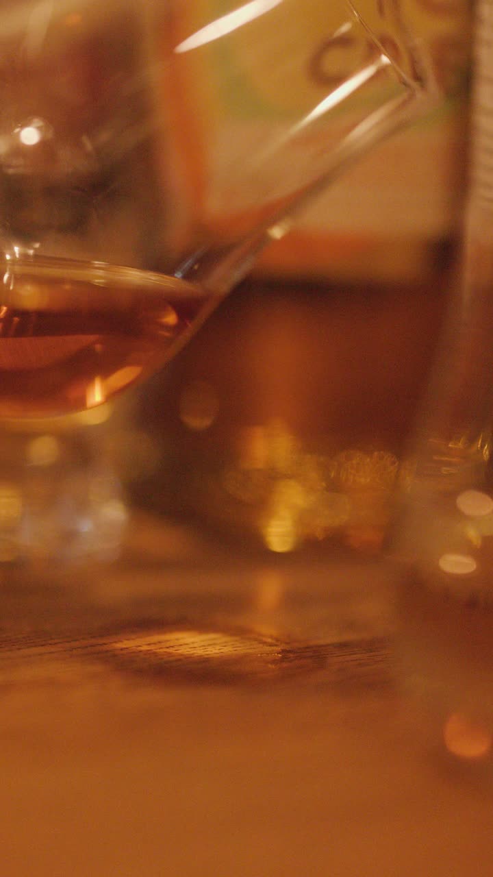 Un primo piano di un bicchiere di whisky delicatamente agitato a mano su un tavolo di legno, con illuminazione ambientale morbida e calda e messa a fuoco ridotta.