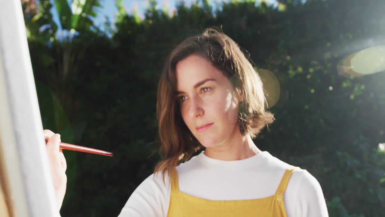 mujer caucásica con cabello marrón pintando en un jardín soleado