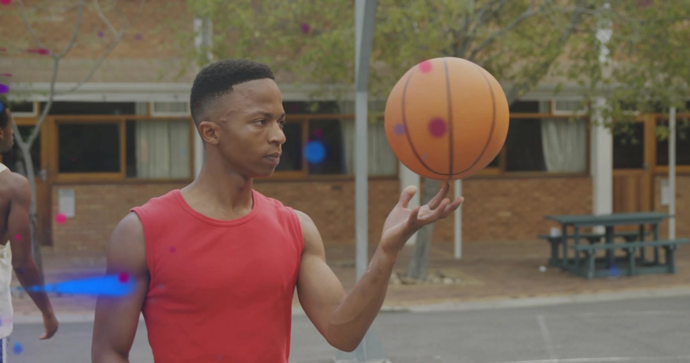 Uomo con maglietta rossa che muove un pallone da basket arancione, facendolo girare sulla punta delle dita mentre si allena, con particelle che fluttuano intorno.