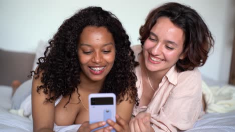 smiling young diverse girlfriends browsing smartphone in daylight