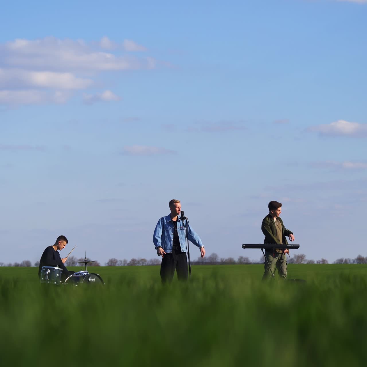 Emotional and active performance of a boys band in the green fields. Music band playing music and sing while drone flying around them