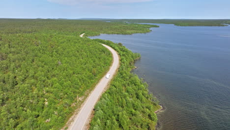 Aerial-view-of-a-Camper-van-driving-at-a-arctic-lake-in-wilderness-of-the-north