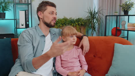 Young-man-father-having-trustworthy-conversation,-talking-with-daughter-child-kid-at-home-sofa