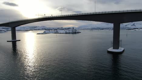 drone view in tromso area in winter flying next to a bridge connecting two islands full of snow over the sea in norway