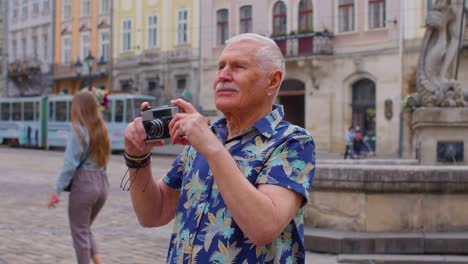 senior man tourist taking pictures with photo camera in summer city center, life after retirement