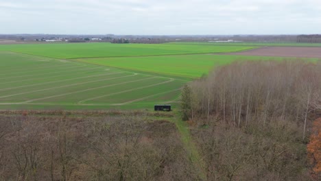 Aerial-View-Of-Off-Grid-Sustainable-Wood-Cabin-On-Corner-Of-Green-Agricultural-Field-In-Belgium