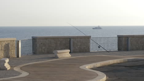 Fishing-Rod-at-the-Empty-Quay-with-Yacht-in-the-Sea,-Sunrise,-Static