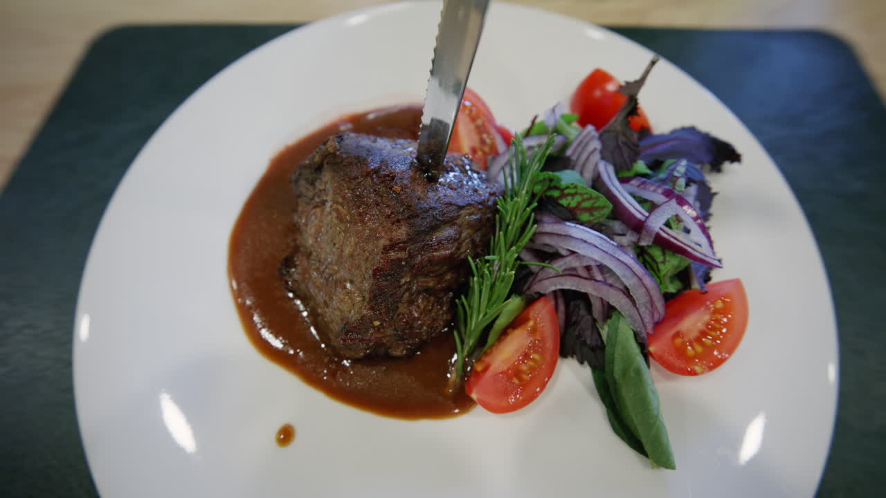 Nahaufnahme eines Gourmet-Fleischgerichts, serviert mit Soße und frischem Gemüse.