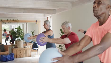 Focused-diverse-seniors-exercising-holding-balls-in-pilates-class,-unaltered,-in-slow-motion