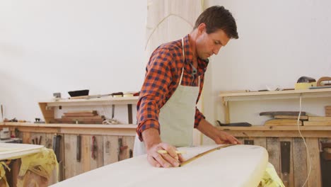 caucasian male surfboard maker checking a surfboard after polishing