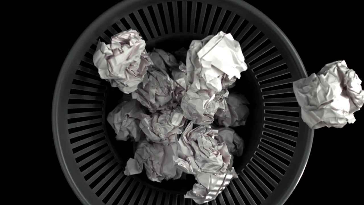 Crumpled Paper Balls Falling into a Wastebasket on Black Background