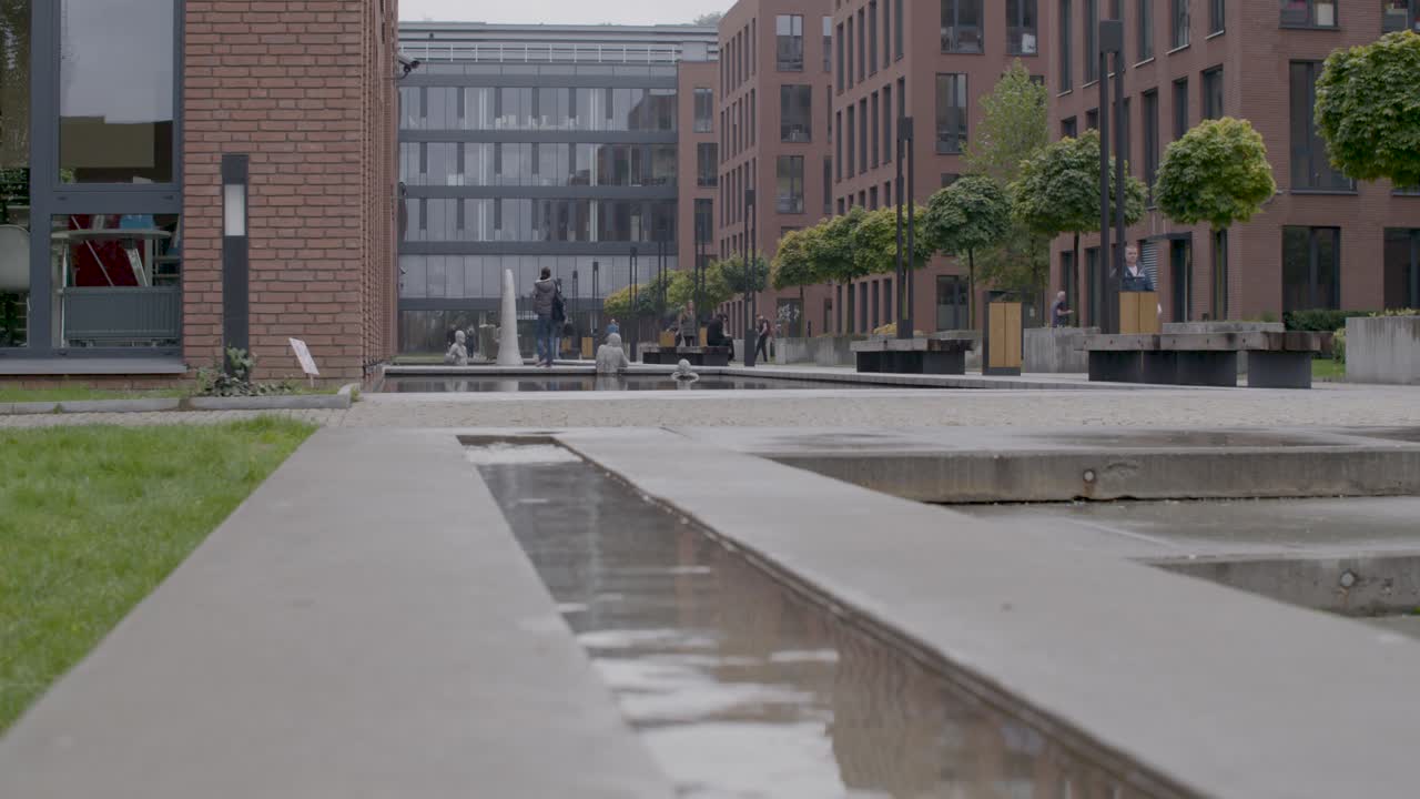 Modern urban plaza with people walking and sitting by a fountain on a cloudy day