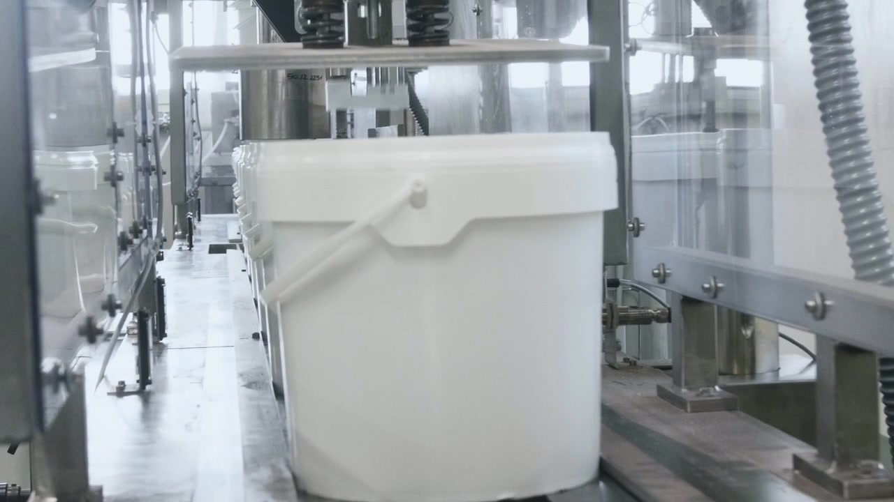 Secchi di plastica bianchi che si muovono attraverso una linea di confezionamento automatizzata avanzata all'interno di una luminosa fabbrica industriale di trasformazione alimentare con macchinari e attrezzature moderne