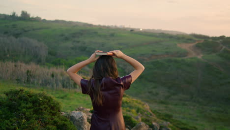 woman putting book head standing green valley. back view girl walking down slope