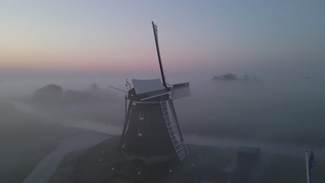 Circling-around-traditional-wooden-windmill-with-stationary-blade,-mist