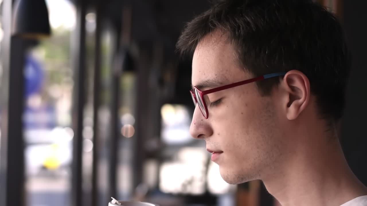Man in red glasses drinking coffee from reusable bamboo cup with a picture of green earth and quote about ecology in a cafe
