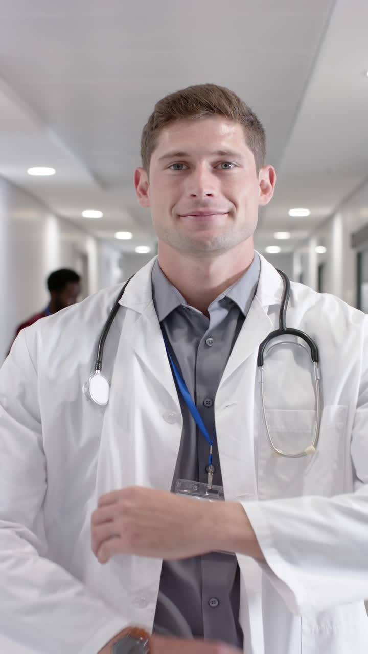 Vertical video of portrait of happy caucasian male doctor looking at camera in slow motion