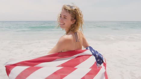 Vorderansicht-Einer-Kaukasischen-Frau-Mit-Wehender-Amerikanischer-Flagge,-Die-Am-Strand-Tanzt,-4k