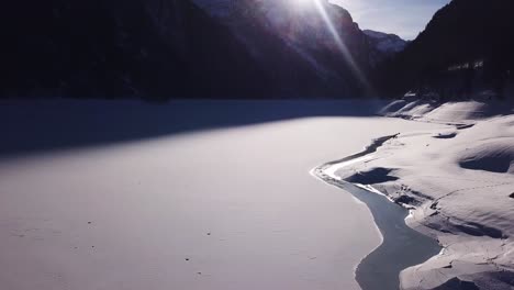 Beautiful-aerial-shot-over-a-frozen-mountain-lake,-tilting-up-to-see-the-big-valley-with-huge-snowy-mountains-in-Klöntal,-Switzerland