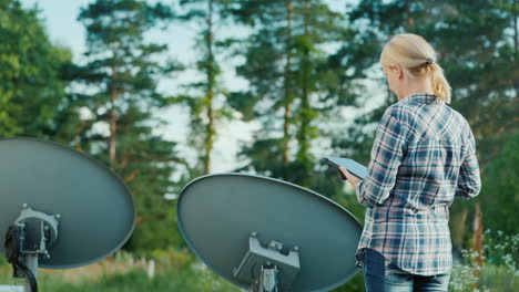 woman tunes satellite dishes outdoors uses tablet