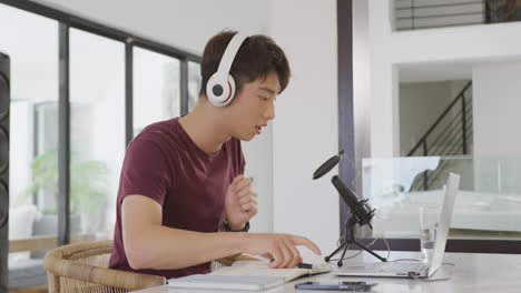 asian boy wearing headphones speaking on professional microphone to record audio podcast at home