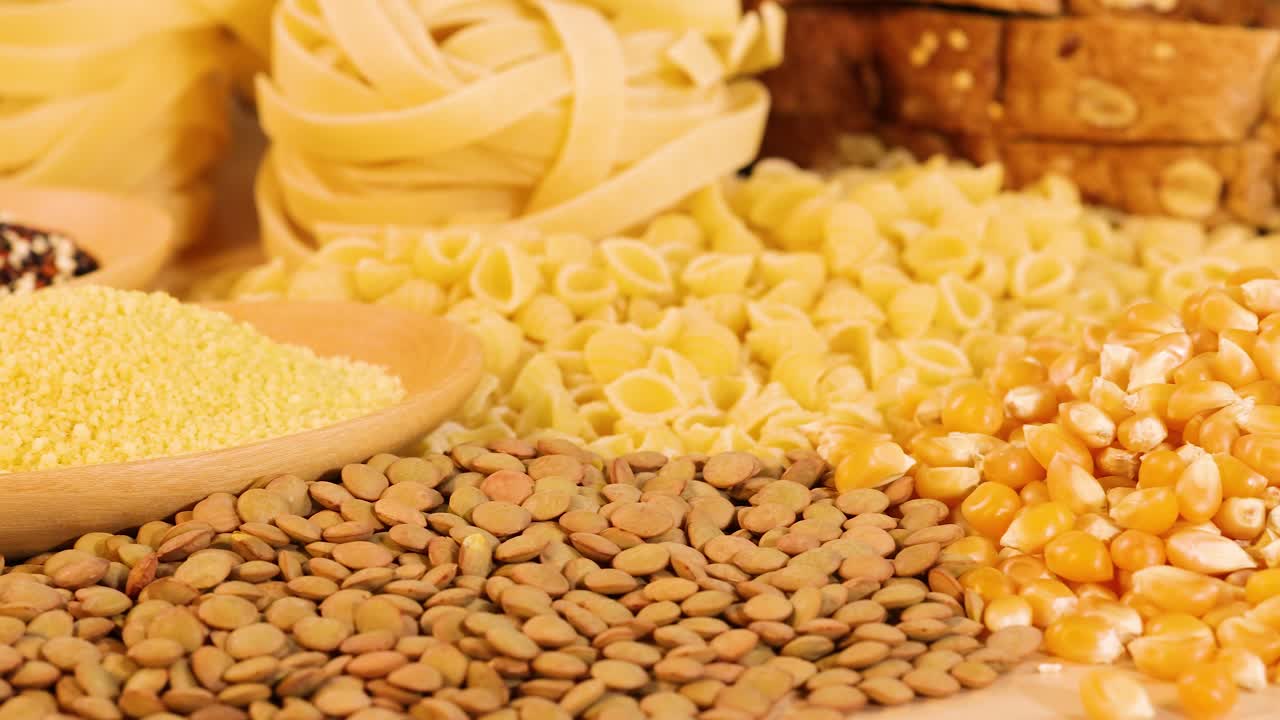 A variety of grains and pasta are artfully arranged, highlighting textures and colors under warm lighting