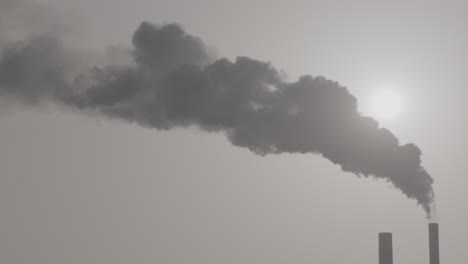 wide slowmotion shot of industrial smoke from a chimney going up in the air with the sun shining through in the background log