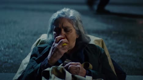an elderly woman lies on a sidewalk at night, clutching a snack in her hands. her expression reflects calmness amid the bustling city, illuminated by streetlights.