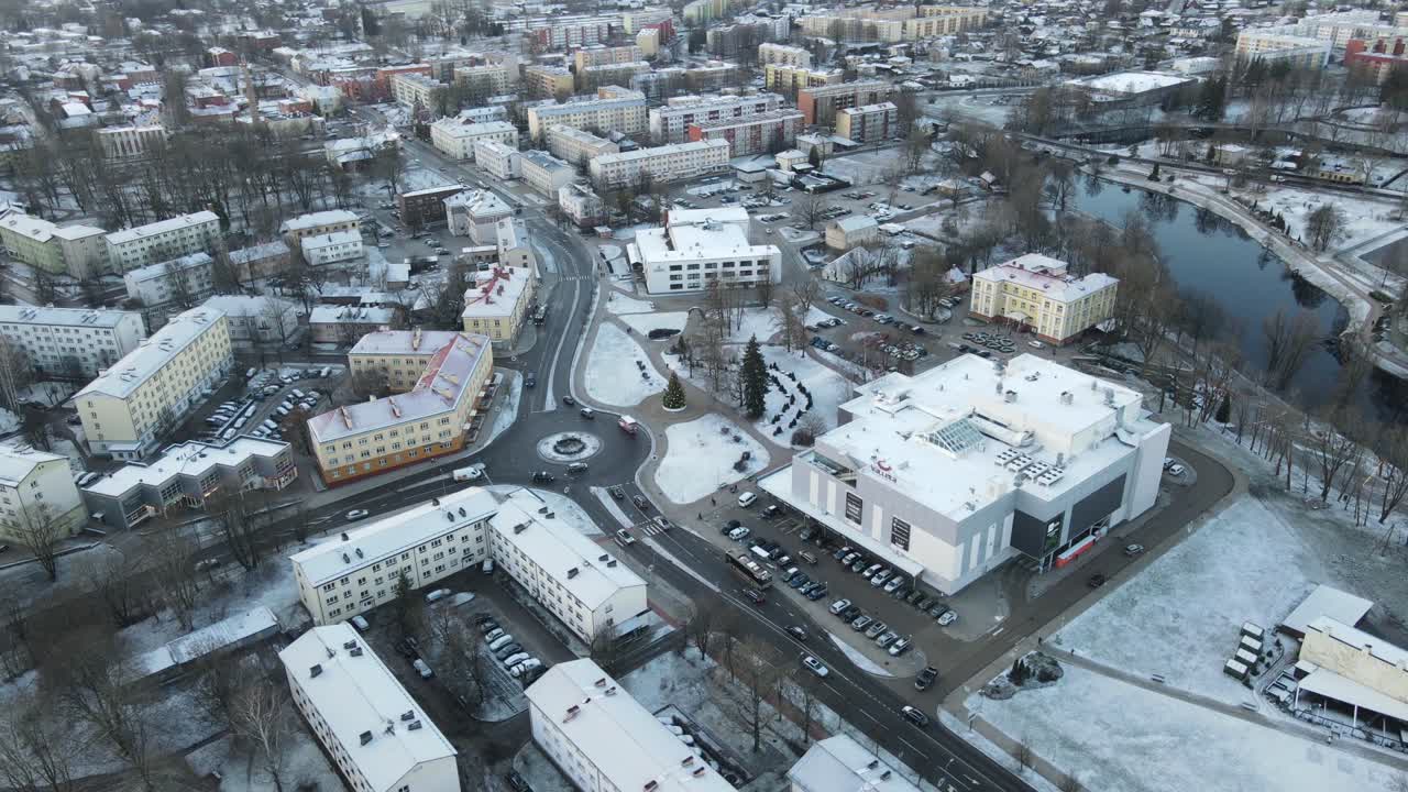 A breathtaking aerial view of Valmiera city, showcasing the winding Gauja River surrounded by snow-covered landscapes and residential areas under a wintry sky.