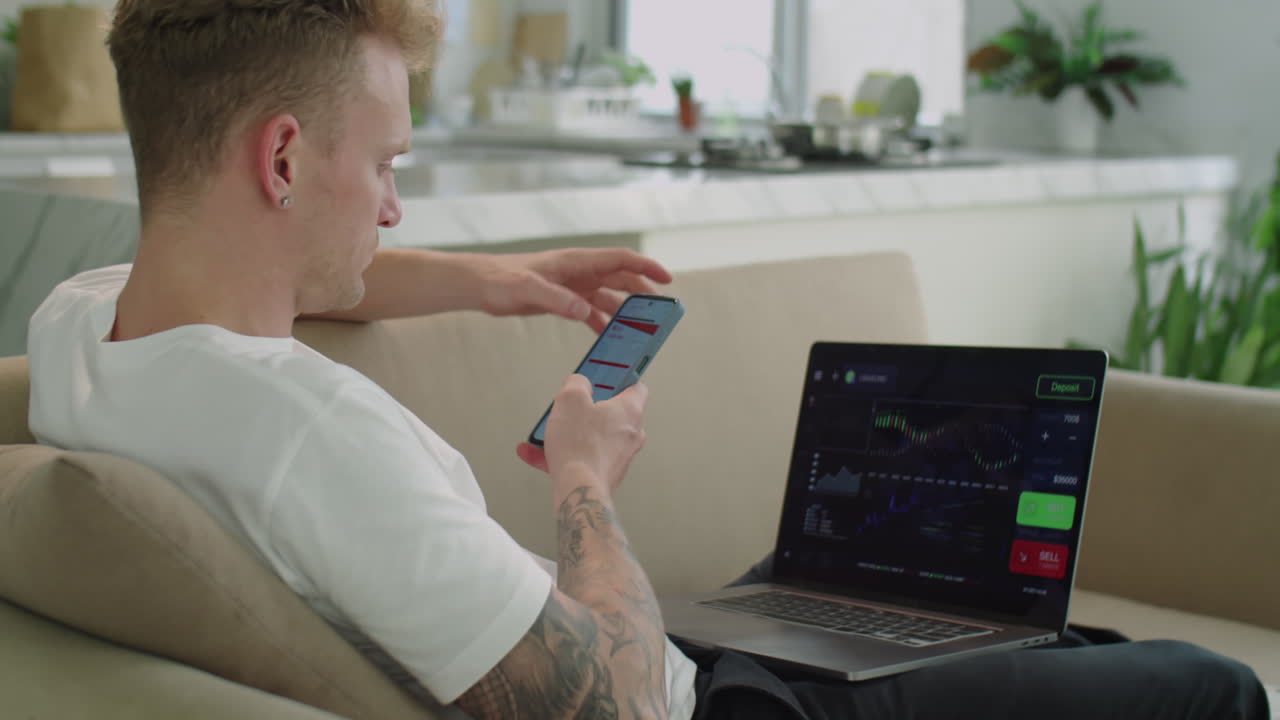 Young Man Using Laptop and Mobile Phone for Online Trade at Home