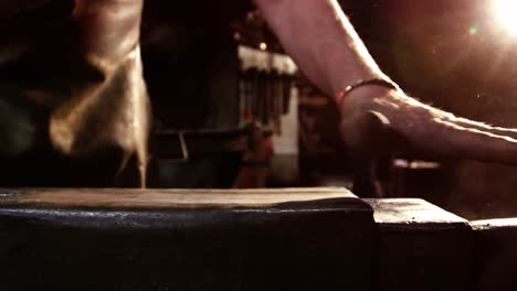 Mid-section-of-blacksmith-cleaning-dust-from-anvil