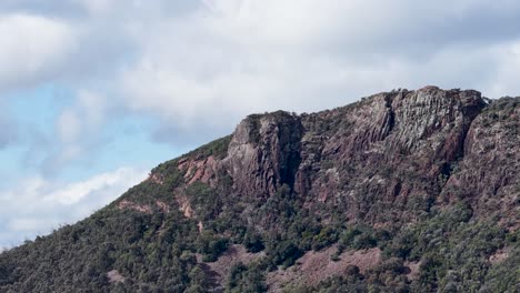 a slow horizontal pan reveals a rugged, tree-lined mountain under partly cloudy skies in coonabarabran, new south wales, with natural daylight and steady camera movement