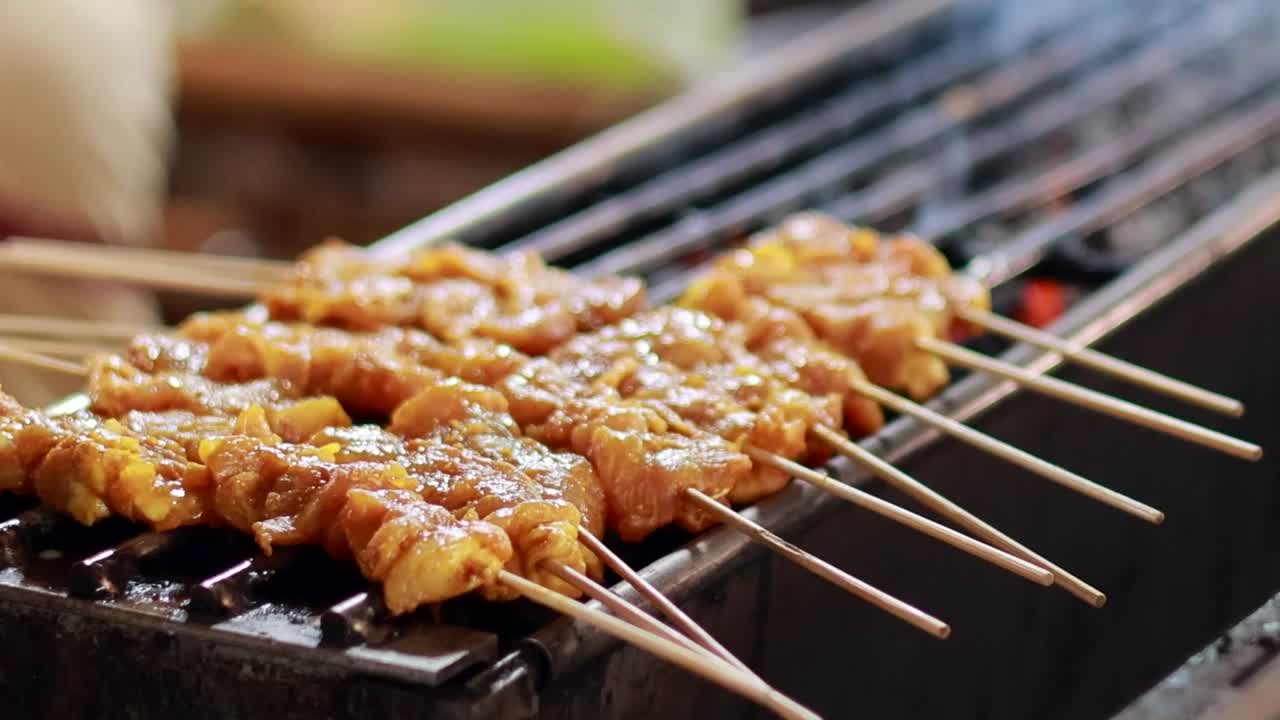 Detailed view of skewered meat grilling over charcoal with visible smoke and glistening marinade.