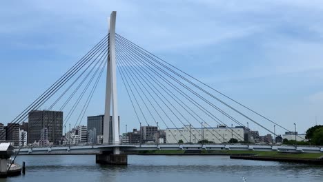 suspension bridge over calm water with cityscape backdrop under a clear blue sky