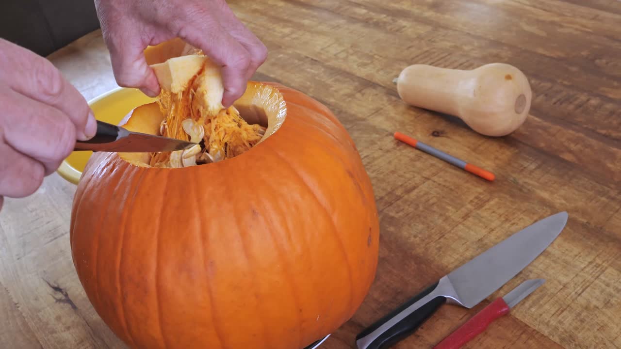 Man scooping out pumpkin seeds and pulp by hand during Halloween carving