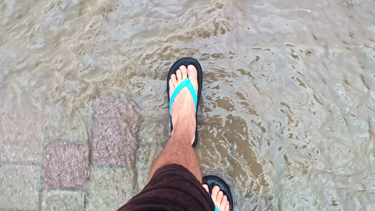 First-person view of flip-flops stepping through flowing puddles on a rain-soaked walkway