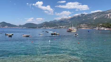 still water surrounding the island of sveti stefan in montenegro on a beautifully sunny day with the high mountains over the water filled with boats