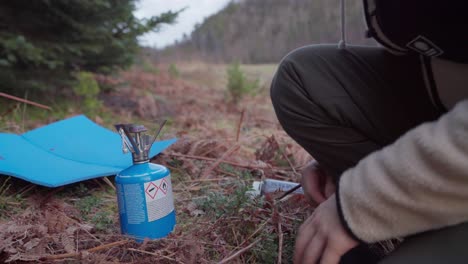 el hombre con un quemador portátil para acampar está hirviendo agua cerca de las montañas del bosque