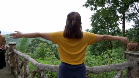 woman in a yellow shirt stretches out her hands welcoming the beautiful this misty morning from her back revealing fantastic scenery and a healthy experience