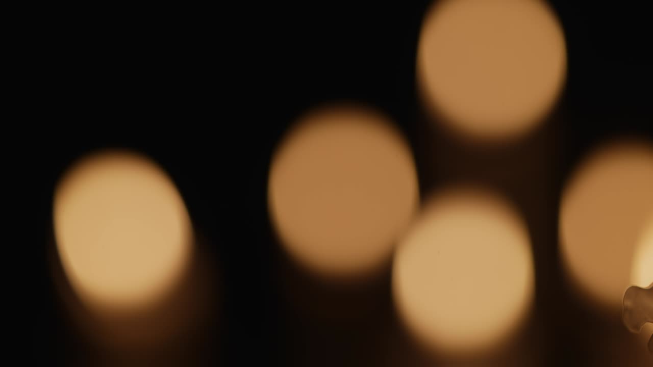 Ett brinnande vaxljus flimrar i mörkret på en svart bakgrund med suddig bokeh-effekt från stearinljus. Bakgrund eller illustration för minne, sorg eller firande. Brinnande ljus i kyrka, närbild.