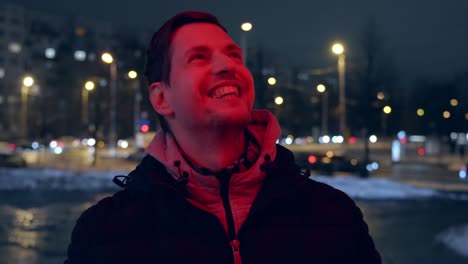 un joven entusiasta y feliz sonriendo bajo los semáforos rojos de la calle en la ciudad
