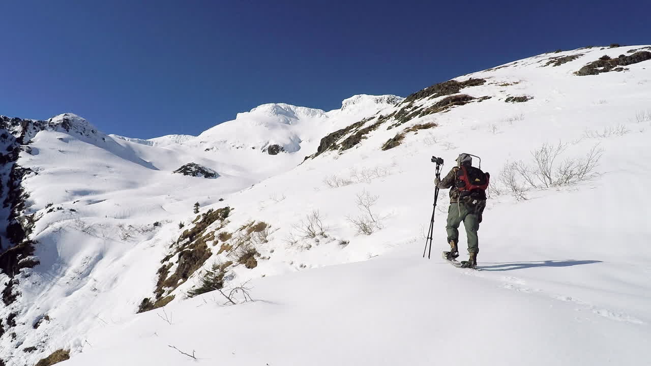 A nature and wildlife photographer snowshoes up the snow covered mountains of Kodiak Island Alaska in preparation for a photoshoot