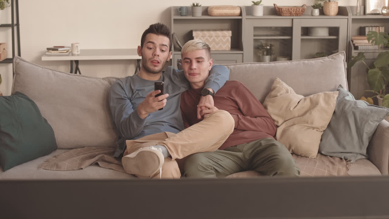Due giovani uomini seduti abbracciati che guardano la TV