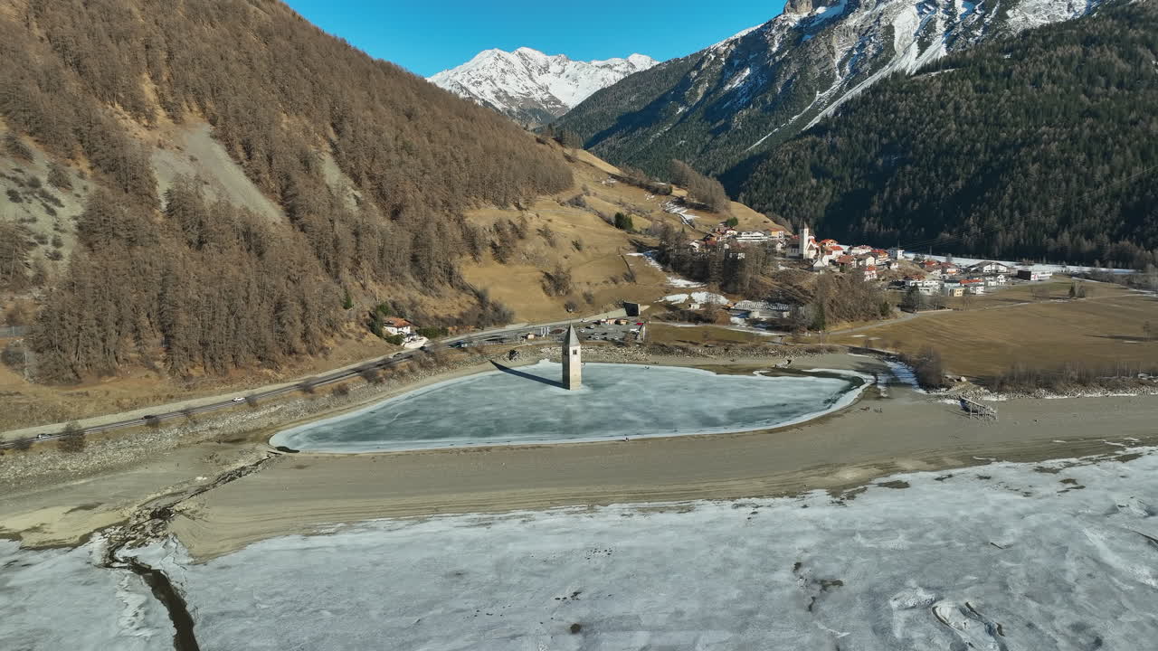 이탈리아의 얼어붙은 호수에 가라앉은 그라운 교회의 드론 돌리 샷