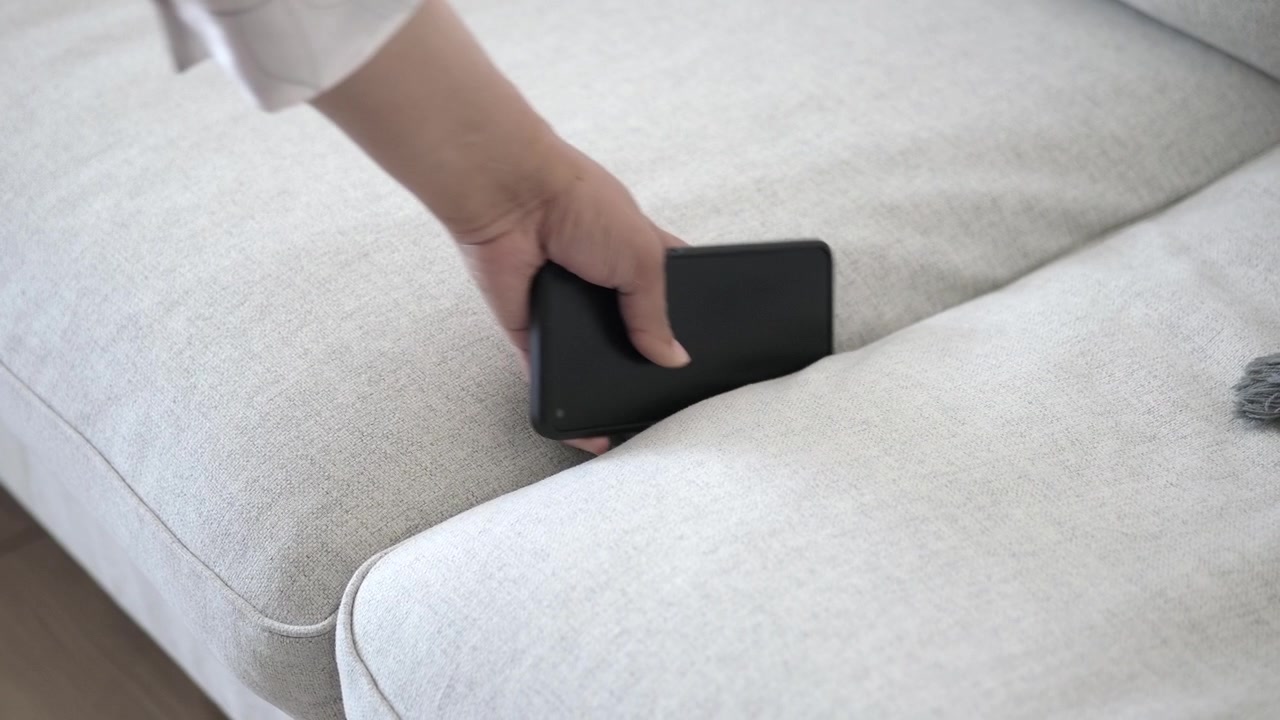 Hånd der fisker en tabt smartphone op fra mellem sofapuderne