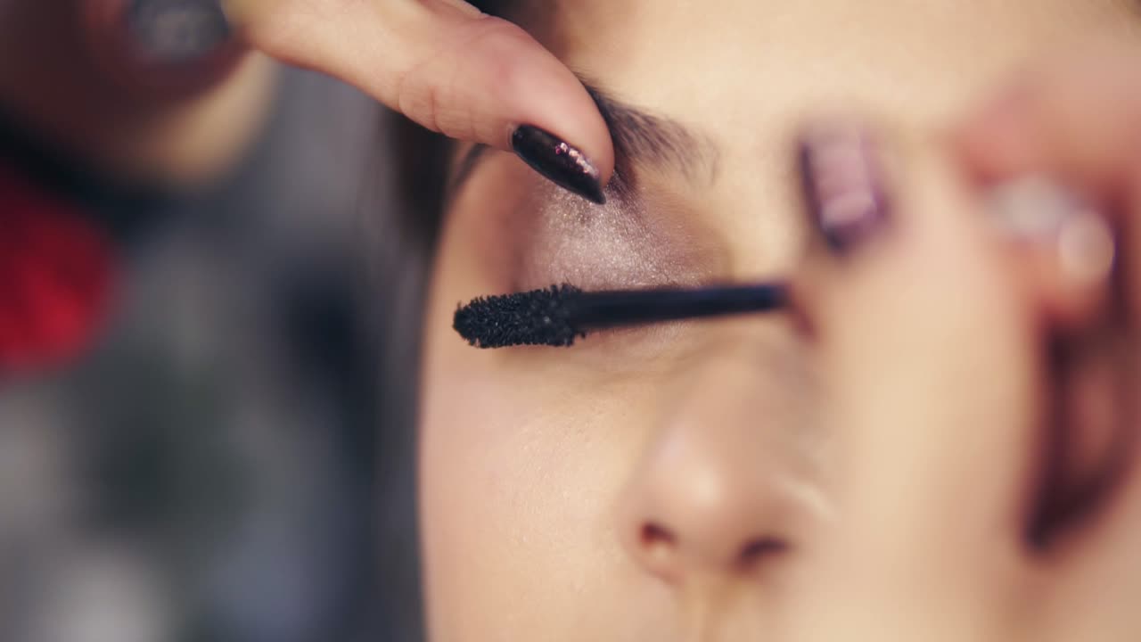 Close Up view of professional makeup artist applying mascara on the model's eyelashes. Work in beauty fashion industry. Backstage