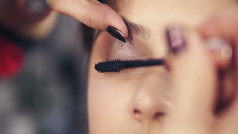 close up view of professional makeup artist applying mascara on the model's eyelashes. work in beauty fashion industry. backstage