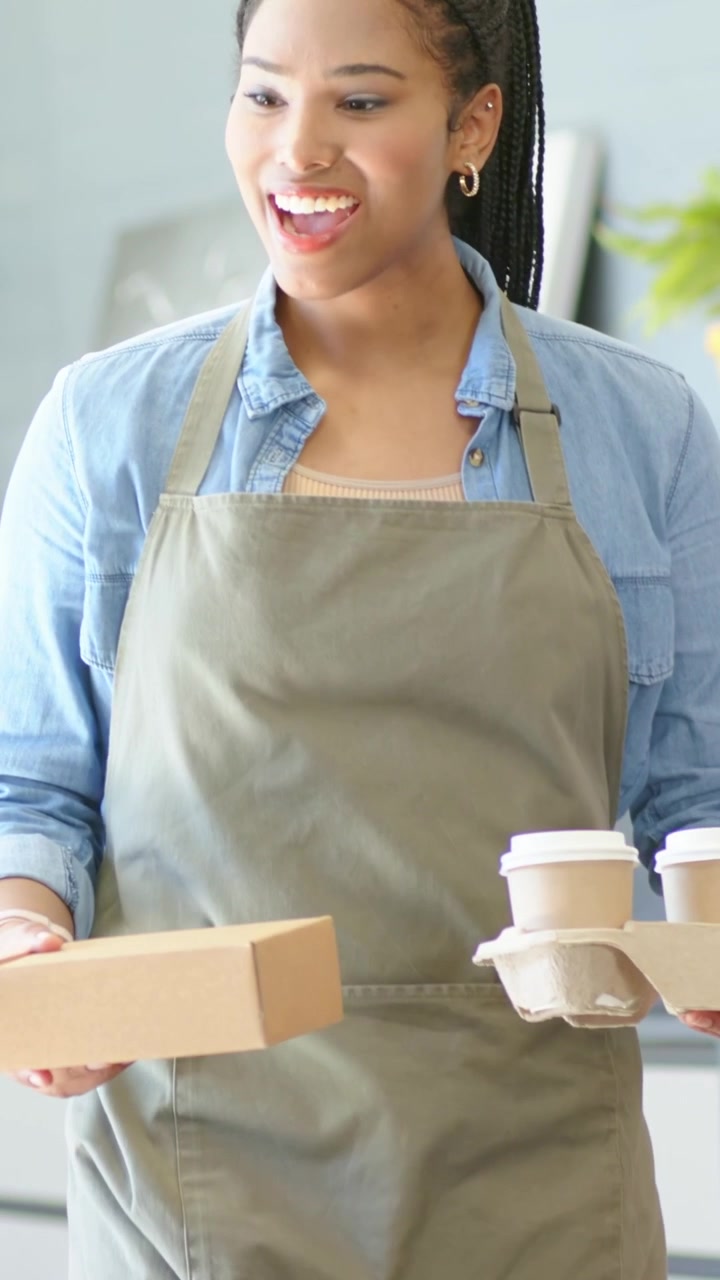 Barista che saluta il cliente dopo aver preso l'ordinazione, posizionando una scatola di cartone e due tazze sul tavolo.